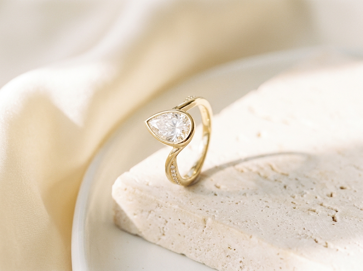 A tight macro view of an oval engagement ring, the pave band in sharp focus on pale travertine