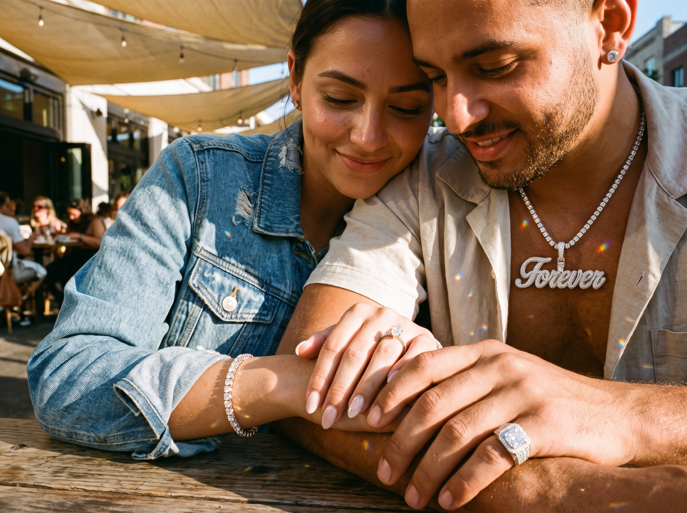 A candid embrace as the couple glance down at their hands, her marquise diamond ring and tennis bracelet and his large diamond ring catching the light, his diamond tennis chain with an iced-out nameplate pendant and a diamond earring